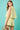 Woman wearing a light green layered outfit against a teal background