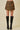A model wearing a brown and black zebra-print wrap mini skirt with black knee-high leather boots, standing against a solid beige background.