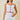 A woman modeling a white two-piece outfit consisting of a spaghetti-strap crop top with scalloped edges and red piping, paired with a matching high-waisted mini skirt with scalloped hem and red contrast stitching.