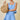Woman in a light blue dress holding a woven bag against a beige background