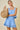 Woman in a light blue dress holding a woven bag against a beige background