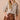 A woman modeling a brown and beige gingham long-sleeve blouse with a ruffled collar and button front, paired with a brown ruffled mini skirt, against a solid beige background.