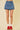 Person wearing a blue denim skirt with red sneakers on a beige background