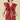 A woman modeling a sleeveless, deep burgundy faux-leather mini dress with dramatic ruffled shoulder details and a gathered front, set against a solid beige background.