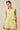 Woman wearing a yellow lace outfit with sunglasses on her head against a beige background