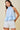 Woman wearing a light blue top and white shorts on a beige background