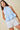 Woman wearing a light blue halter top with ruffled details and white shorts on a beige background