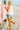 Woman in a white top and denim shorts standing on a sandy beach next to a pink vehicle.
