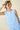 Woman wearing a light blue sleeveless top with lace details on a beige background