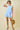 Woman wearing a light blue sleeveless top and shorts set, holding a woven bag on a beige background