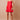 A woman modeling a bright red spaghetti-strap mini dress with a gathered bow detail at the bust and a button-front overlay, photographed against a solid warm beige studio backdrop.