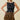 A woman modeling a sleeveless black smocked crop top with a ruffled hem and a matching smocked tiered mini skirt featuring a brown and black zebra print, set against a solid beige background.