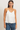A woman modeling a white satin camisole top with thin spaghetti straps and a V-neckline, paired with blue jeans, against a plain off-white studio background.