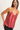 A woman modeling a shiny, metallic rose pink spaghetti-strap camisole top against a plain off-white background.