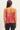 A woman shown from the back wearing a shiny coral pink spaghetti-strap camisole top and black leggings against a plain light background.
