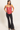 A woman modeling a shiny coral pink satin camisole top paired with black flared pants and black flats, standing against a plain light background.