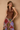 A woman posing in a brown satin halter top and a colorful patchwork print skirt against a textured beige wall.