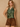 A woman modeling a sleeveless olive green satin halter top with a draped cowl neckline, paired with brown suede-like drawstring shorts, set against a textured beige studio backdrop.