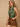 A woman modeling a sleeveless olive green satin halter-style top paired with brown shorts, standing against a textured beige wall.