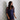 A woman wearing a sheer navy blue sequined mini dress with mesh sleeves, standing against a light gray and white patterned wallpaper background.