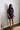 A woman wearing a navy blue sequined mesh mini dress with sheer elbow-length sleeves, standing against a patterned wallpaper background.