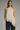 Woman wearing a beige halter top with lace trim and black pants on a gray background