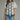 Woman wearing a white blouse with black embroidery and blue jeans on a gray background