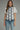 Woman wearing a white blouse with black embroidery and blue jeans on a gray background