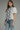 Woman wearing a white blouse with black embroidery and blue jeans on a gray background