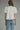 Woman wearing a white blouse with black embroidery and light blue jeans on a gray background