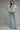 Woman wearing a white blouse with black embroidery and blue jeans on a gray background