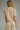 A woman shown from the back wearing a short-sleeve knit polo-style top and matching light beige trousers against a plain gray studio background.
