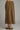A brown suede midi skirt shown from the back on a model, paired with brown strappy heels, against a solid gray studio background.