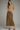 A woman modeling a beige cable-knit short-sleeve sweater and a brown suede midi skirt with front patch pockets and gold-tone chain accents, photographed against a plain light gray studio background.