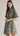 A woman modeling a short-sleeve high-neck mini dress with a teal background and a vertical floral print in orange, red, and green, set against a plain light gray studio background.