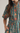 A close-up of a woman wearing a teal short-sleeve shirt dress with a red and orange floral print and a matching tie belt, shown against a plain light background.