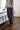 A woman wearing a gray short-sleeve knit top with white polka dots, dark gray wide-leg jeans, and red flats, standing in a bedroom next to a bed with a wooden floor.