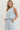 Woman wearing a light blue sleeveless top and pants with floral patterns on a white background
