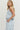Woman wearing a light blue sleeveless top and jeans with floral cut-out details on a white background