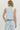 Woman wearing a light blue sleeveless top and pants with floral cut-out details on a white background