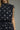 Close-up of a sleeveless high-neck dress with white polka dots on a dark navy blue fabric, featuring tie details on the shoulder straps, worn by a model against a neutral gray background.