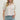 Woman wearing a white blouse with pink embroidery and blue jeans on a plain background