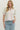 Woman wearing a white blouse with pink embroidery and blue jeans on a plain background