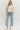 Woman wearing a white blouse with pink embroidery and light blue jeans on a white background