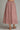 A pink and white gingham midi skirt with dark red polka dots, shown on a model from the waist down wearing gold sandals against a neutral gray background.