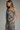 A woman wearing a sleeveless camisole dress with a zebra-like abstract print in black, beige, and gray, posed against a neutral gray studio background.