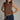 Woman wearing a brown sleeveless top with decorative trim and blue jeans against a gray background