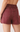 Rear view of a person wearing high-waisted denim shorts in a muted burgundy or wine tone, with two large back pockets and a visible waistband.