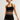 A woman modeling a matching black and white athletic set consisting of a ribbed sports bra, a high-waisted tennis skirt with white stripes, and a black headband with a small white logo, against a plain light gray studio background.