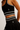 Close-up of a model wearing a black ribbed two-piece activewear set with white stripes and a small silver leaf logo, featuring a sports bra and matching high-waisted skort.
